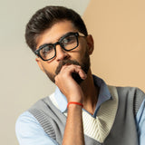 Ares Black Clear Square Sunglasses – Sunglassic.com. Male model in bold black square-frame sunglasses with clear lenses, styled in a smart blue shirt and knitted vest, posing thoughtfully against a soft beige background.