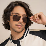 Heldish Gold Black Square Sunglasses – Sunglassic.com. Male model wearing square sunglasses with gold metal frames and black accents, styled in a pastel green shirt and beige tee, posing against a white background.