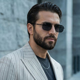 Man wearing sunglasses and a light gray suit against a blurred urban background