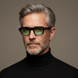 Man wearing black glasses and a black turtleneck against a gray background