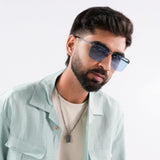 Heldish Black Blue Square Sunglasses – Sunglassic.com. Male model wearing gradient blue-tinted square sunglasses with black rims, styled in a pastel green shirt and beige tee, posing against a white background.