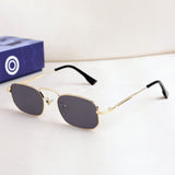 Gold-framed sunglasses with dark lenses on a white surface, with a blue box featuring a white logo in the background.